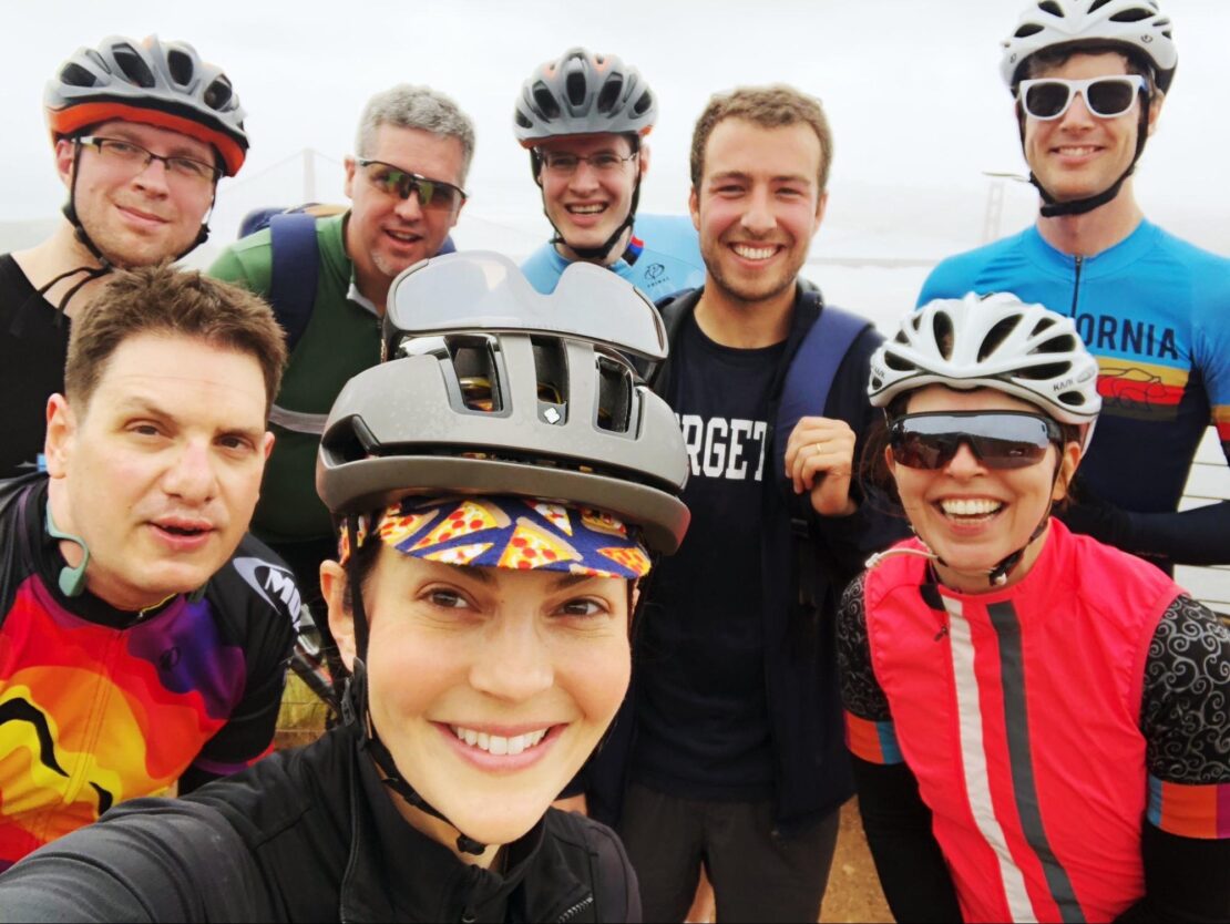 Group photo showing people wearing bike helmets, sunglasses, and riding gear, taken during a pre-conference bike ride at DockerCon 2019 in San Francisco.